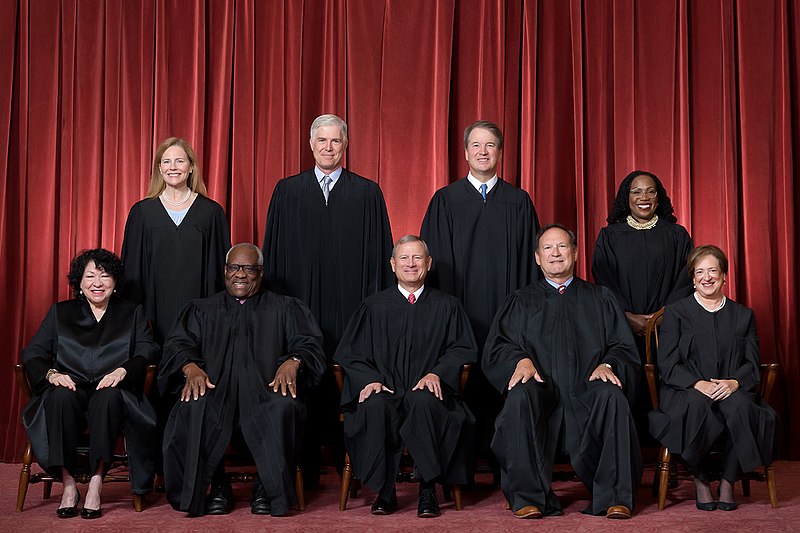 Formal group photograph of the Supreme Court as it was been comprised on June 30, 2022 after Justice Ketanji Brown Jackson joined the Court.  The Justices are posed in front of red velvet drapes and arranged by seniority, with five seated and four standing...Seated from left are Justices Sonia Sotomayor, Clarence Thomas, Chief Justice John G. Roberts, Jr., and Justices Samuel A. Alito and Elena Kagan. Standing from left are Justices Amy Coney Barrett, Neil M. Gorsuch, Brett M. Kavanaugh, and Ketanji Brown Jackson. 